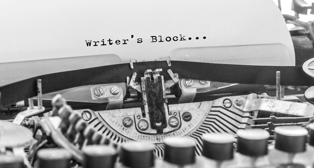 Black-and-white close-up of a vintage typewriter with "Writer's Block..." typed on it.