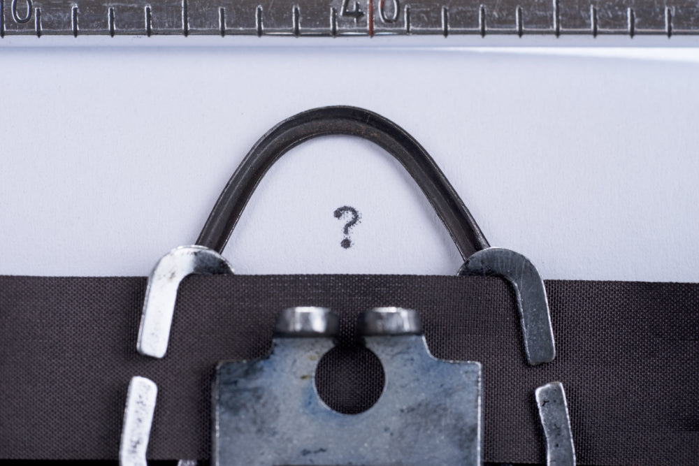 Close-up of a typewriter carriage with a single question mark typed on paper.